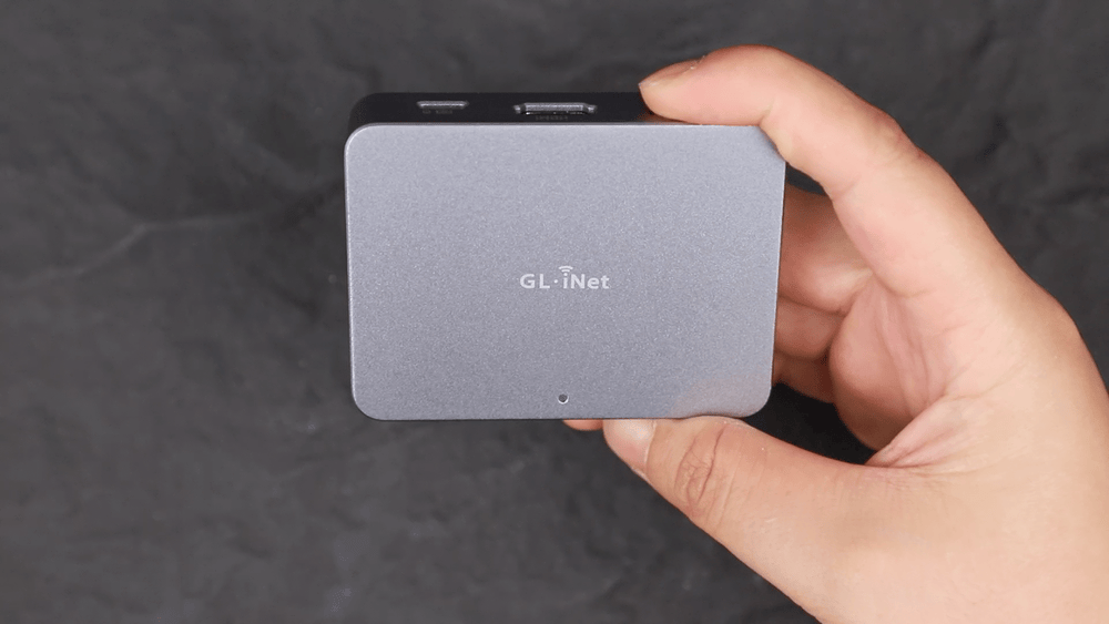 Front and back views of the GL.iNet Comet (GL-RM1) KVM device: the front shows a sleek metallic finish with a logo and LED indicator, while the back reveals technical specifications and anti-slip pads, held in a person’s hand for size reference