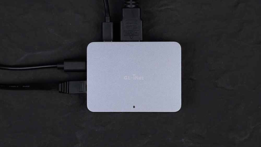 Top view of the GL.iNet Comet (GL-RM1) device fully connected with multiple cables—HDMI, USB, and Ethernet—demonstrating active setup on a dark textured surface.